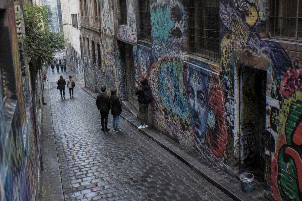 Visitors walking through a narrow Melbourne laneway while a guide points out street art on the wall