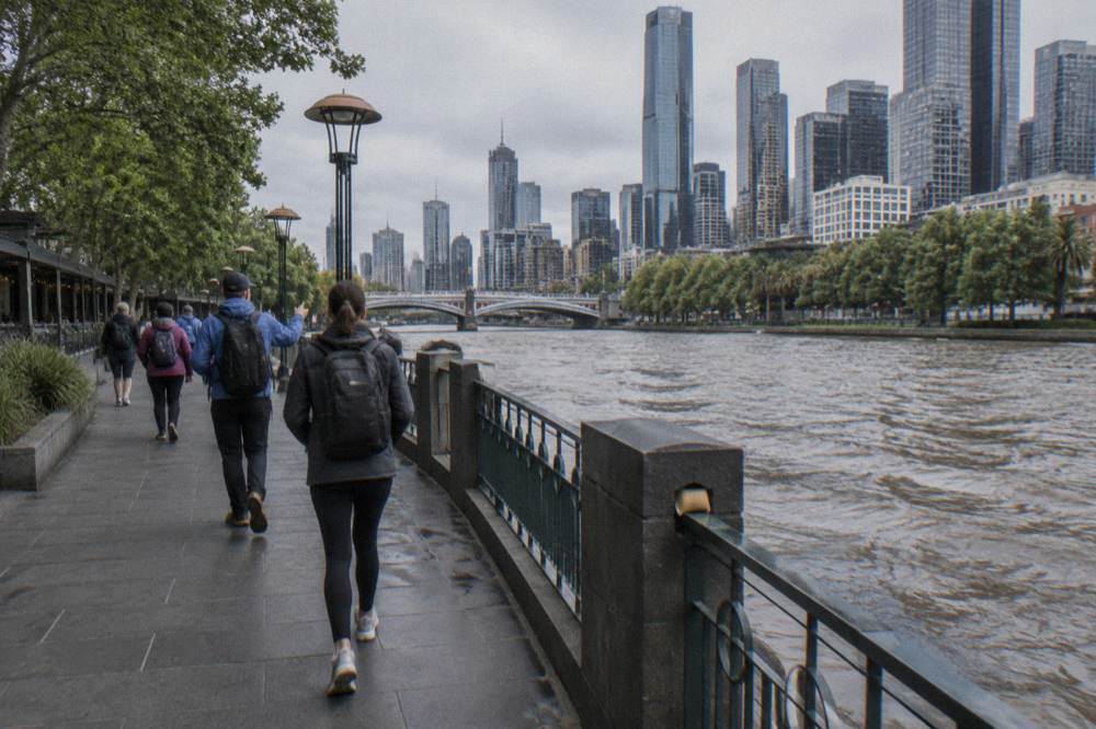 A guide leading a walking group along the Southbank promenade beside the Yarra River with the city skyline behind