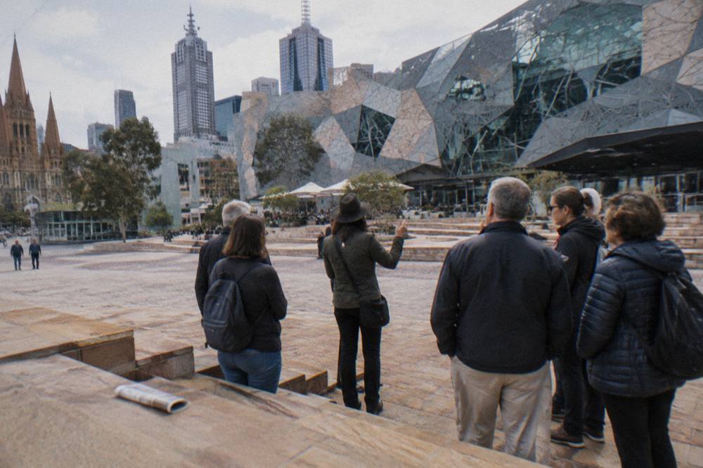 A guide speaking to a small group of adult visitors outside Flinders Street Station under the famous clocks