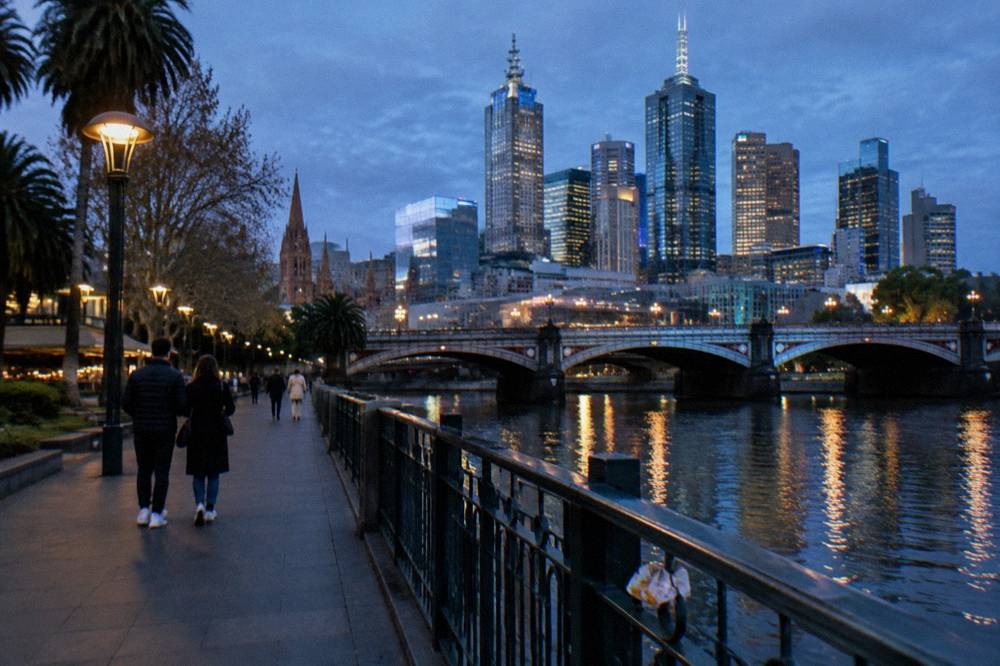 Couples walking along the Southbank promenade at dusk with the Princes Bridge and city lights reflecting in the Yarra River