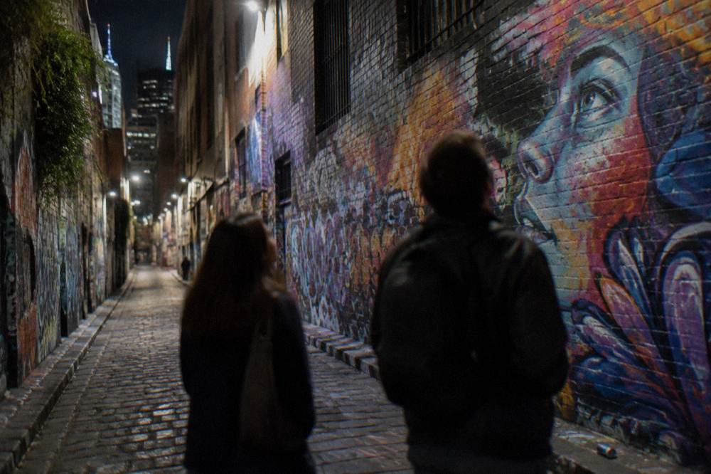 Visitors admiring the ever-changing street art covering the walls of a narrow Melbourne laneway at night