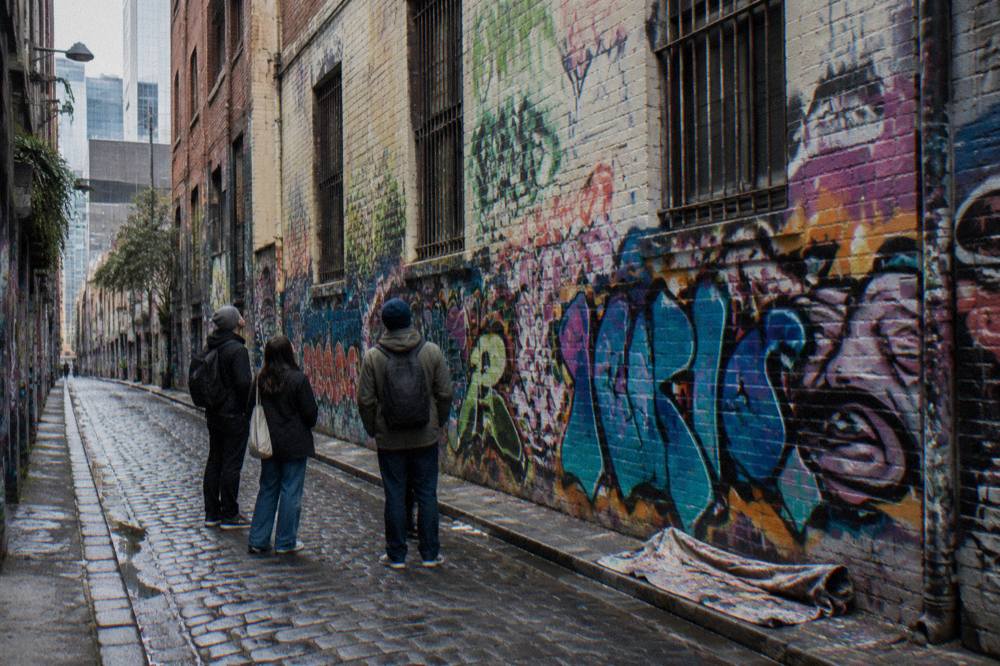 A narrow Melbourne laneway covered in colourful layered street art with a few people looking up at the walls