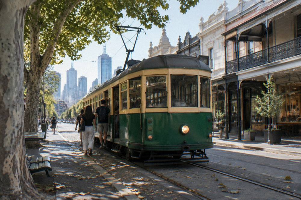 A historic Melbourne tram moving along a city street with passengers boarding