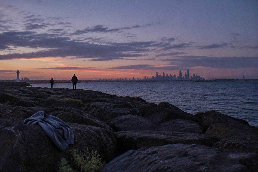 People standing on the St Kilda breakwater at dusk looking out over the water toward the city skyline