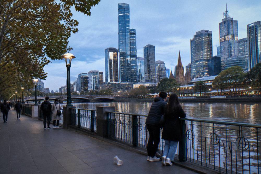 Walkers along the Southbank promenade beside the Yarra River with the Melbourne skyline behind