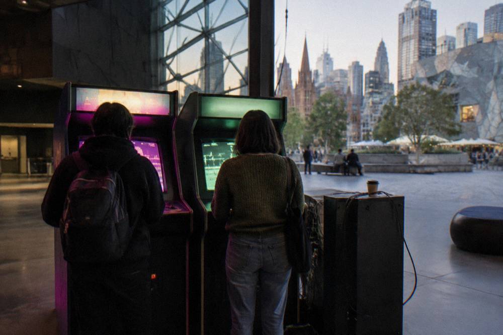 People playing vintage arcade and console games at a free interactive exhibit inside ACMI