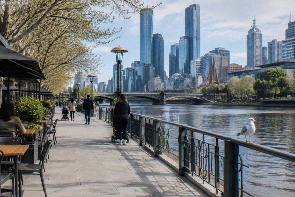 People strolling along the Southbank promenade beside the Yarra River with the city skyline behind them