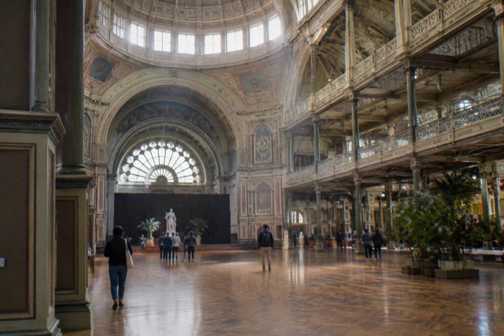 A grand gallery interior with high ceilings and visitors viewing large artworks