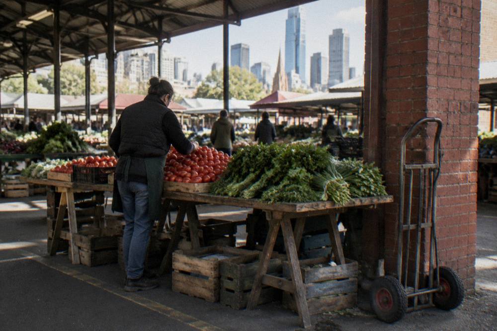 Stallholders arranging fresh vegetables beneath the open heritage shed roof at Queen Victoria Market