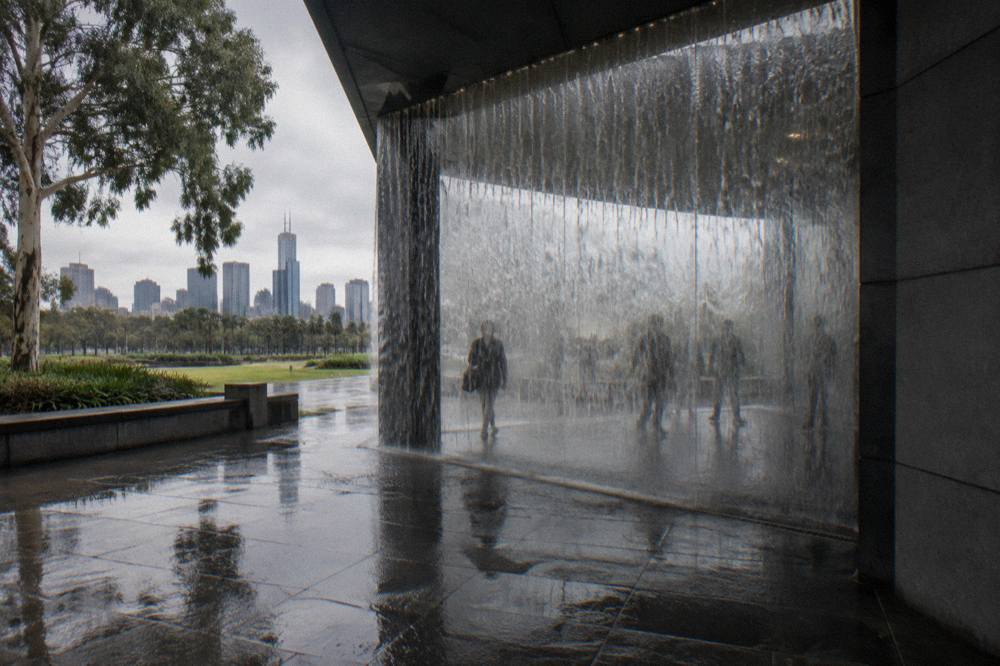 The glass waterwall entrance of NGV International with visitors passing through into the gallery foyer
