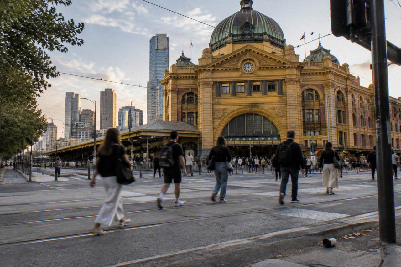 Flinders Street Station facade under a clear sky with pedestrians crossing the intersection in front of it
