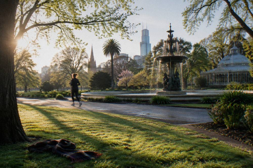 A tree-lined path and open green lawns in Fitzroy Gardens on a sunny day