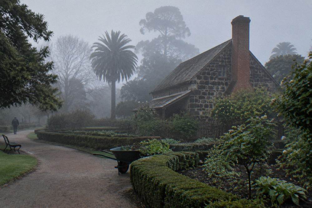 A small historic stone cottage building set among hedges and garden paths