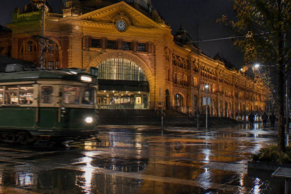 A free City Circle tram passing lit-up Flinders Street Station at night