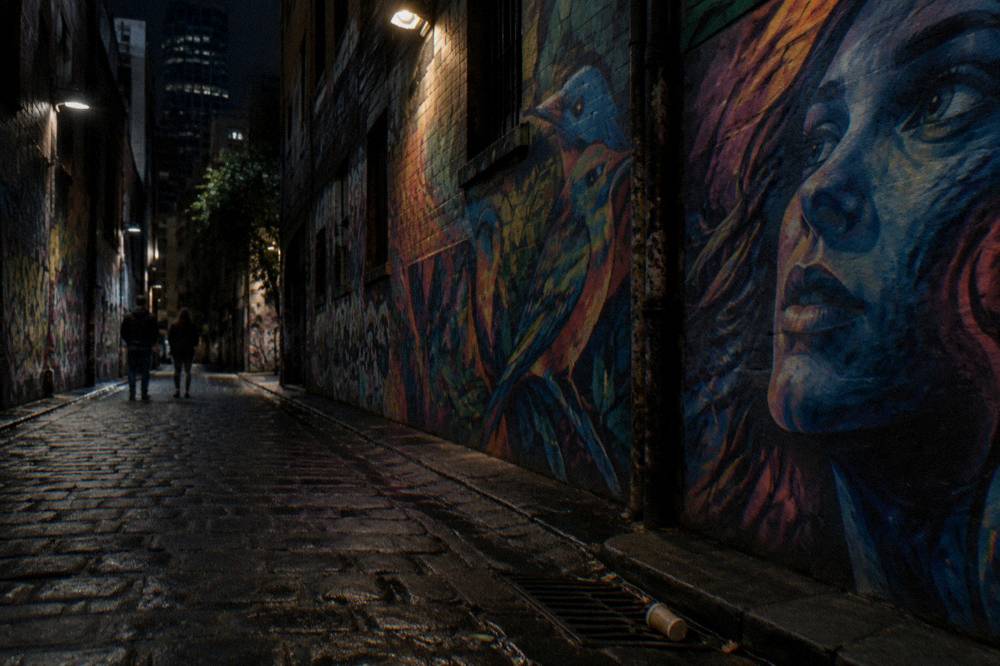 Lit-up street art murals covering the walls of Hosier Lane at night