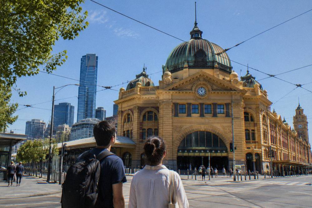 Two people looking up at the Flinders Street Station clock tower and dome from a city intersection