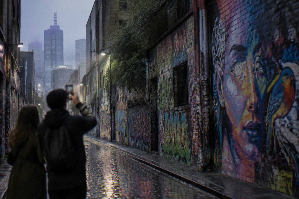 Two people photographing colorful street art covering the walls of a narrow Melbourne laneway