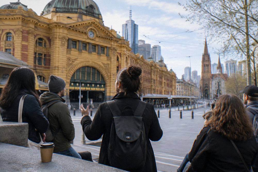 A tour guide holding an umbrella speaking to a small group of visitors outside Flinders Street Station