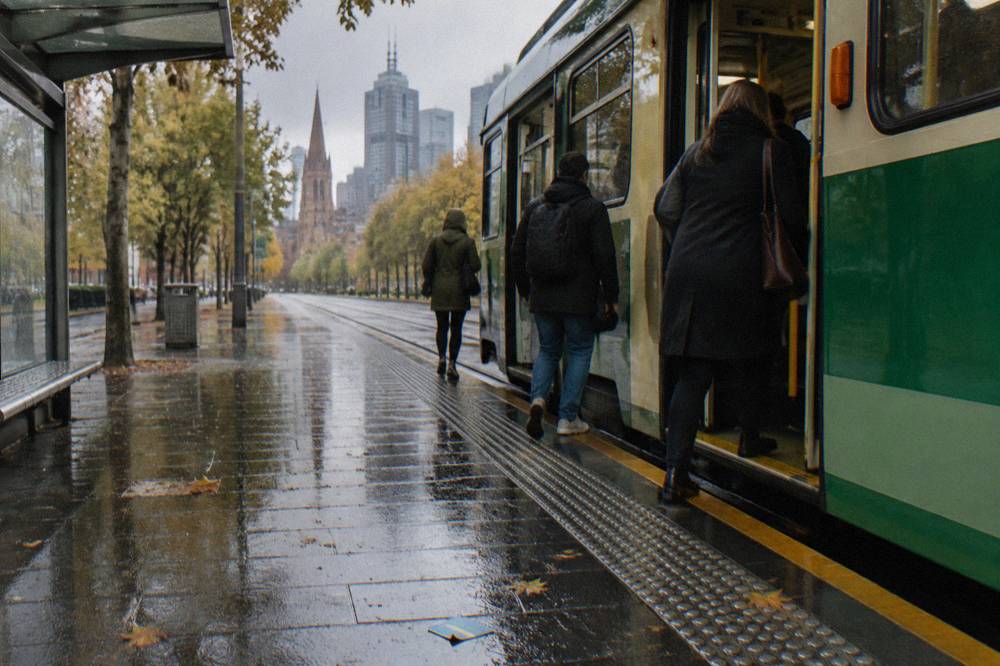 Passengers boarding a tram at a stop on a tree-lined Melbourne city street