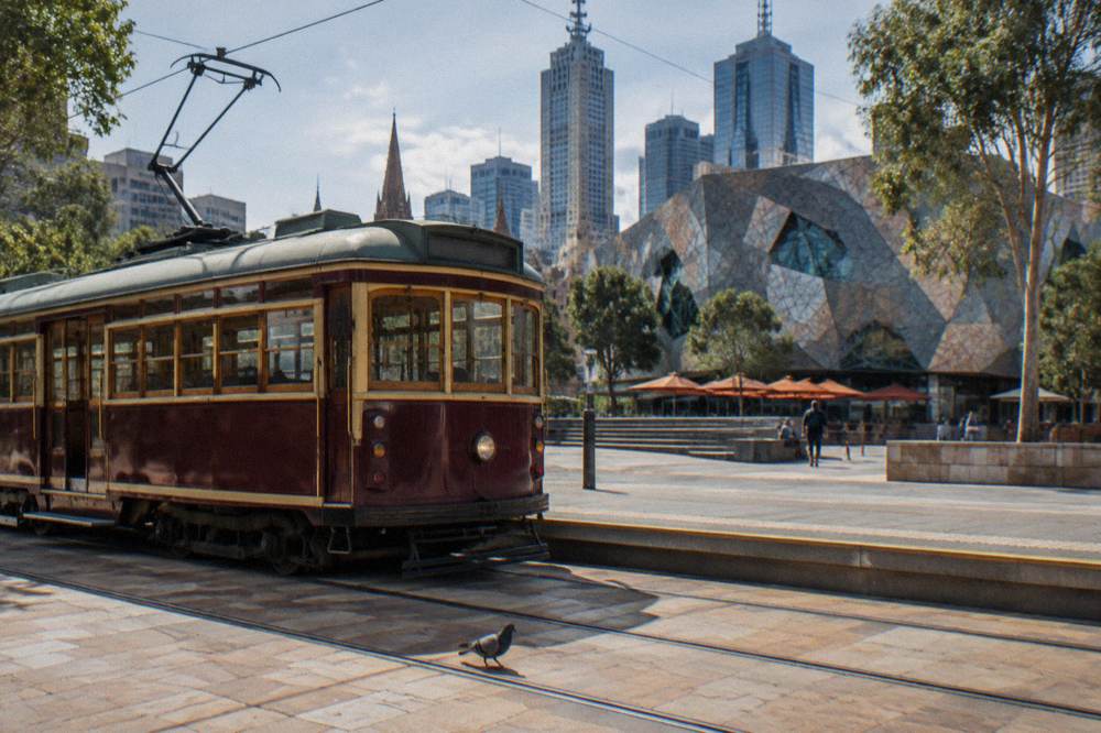 A burgundy heritage City Circle tram at a stop beside a city square