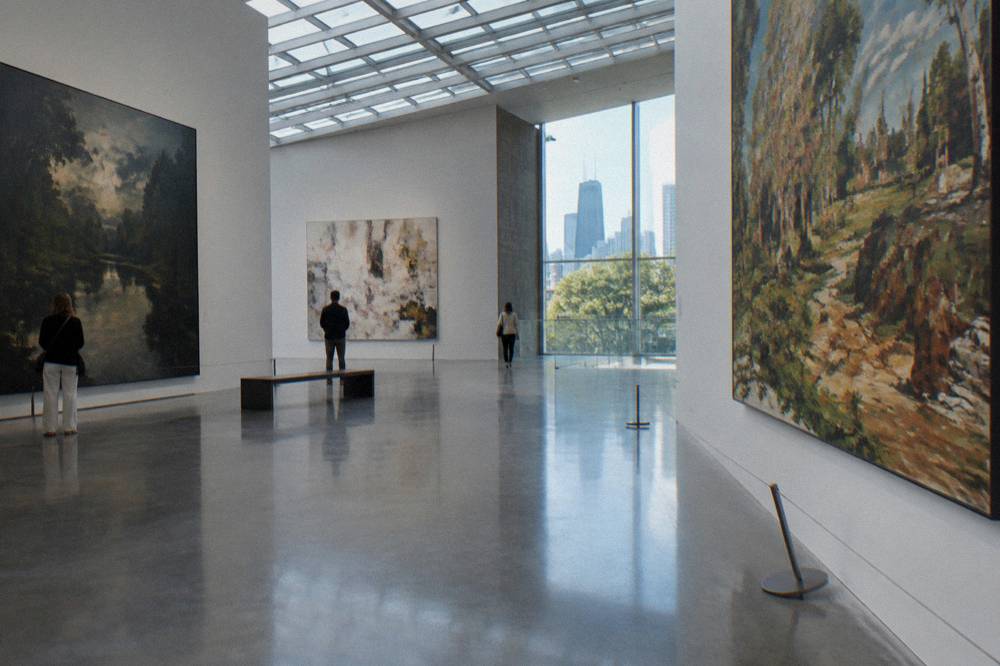 Visitors walking through a bright gallery hall with large paintings on the walls